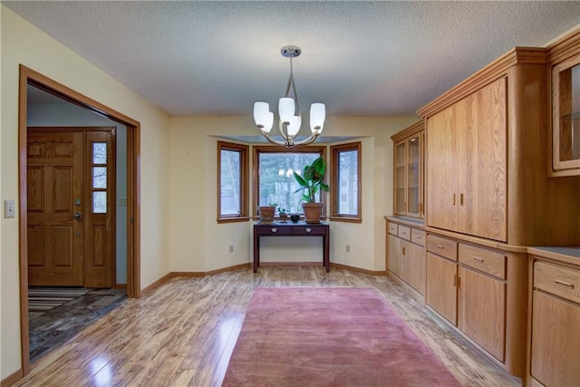 unfurnished dining area featuring a textured ceiling, light hardwood / wood-style floors, and an inviting chandelier