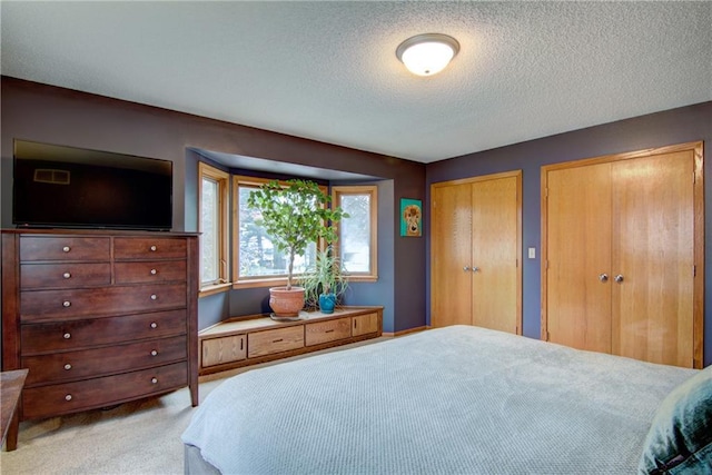 bedroom featuring a textured ceiling, light carpet, and two closets