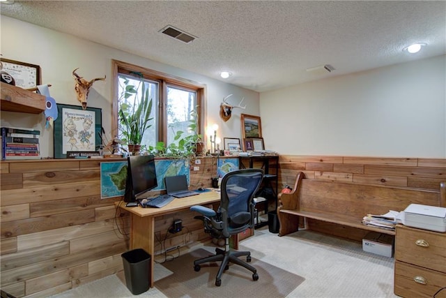 carpeted home office with a textured ceiling and wooden walls