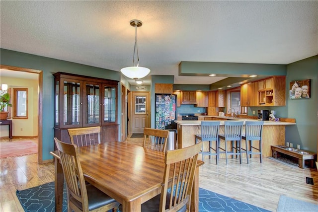 dining space featuring sink, a chandelier, a textured ceiling, and light wood-type flooring