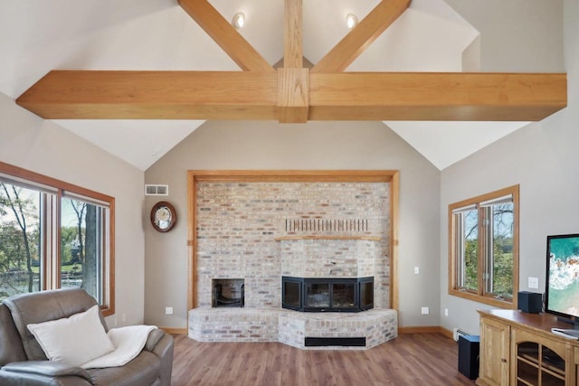 living room with vaulted ceiling with beams, light hardwood / wood-style floors, a brick fireplace, and plenty of natural light