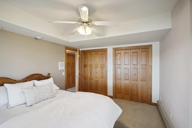 bedroom with ceiling fan, light colored carpet, two closets, and a baseboard heating unit