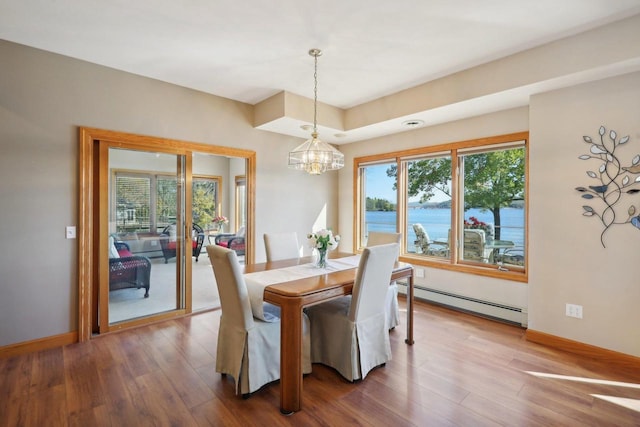 dining area featuring a chandelier, a water view, wood-type flooring, and a baseboard heating unit