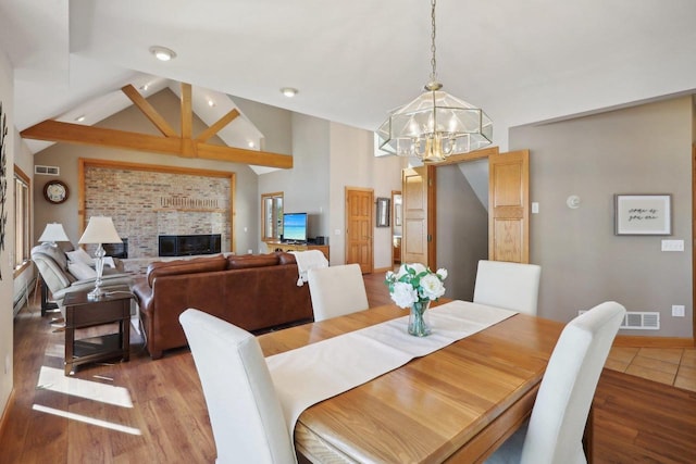 dining space with hardwood / wood-style floors, a notable chandelier, a fireplace, and high vaulted ceiling