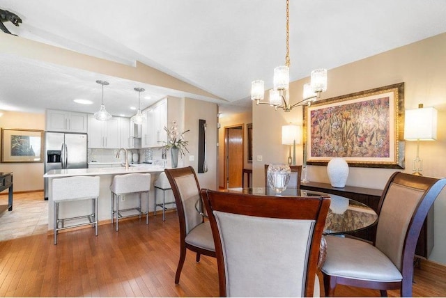 dining space featuring sink, hardwood / wood-style floors, vaulted ceiling, and a notable chandelier