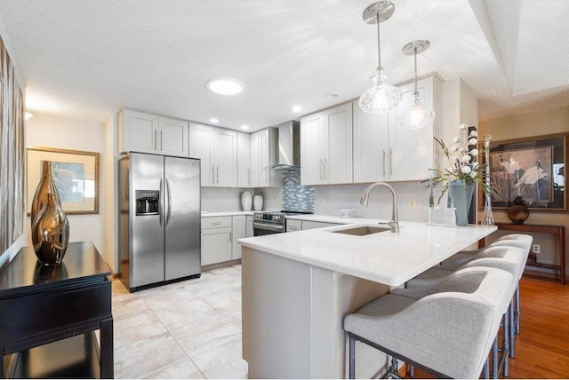 kitchen with appliances with stainless steel finishes, wall chimney exhaust hood, a textured ceiling, sink, and hanging light fixtures