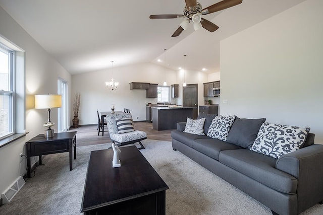 carpeted living room featuring ceiling fan with notable chandelier, vaulted ceiling, and a wealth of natural light