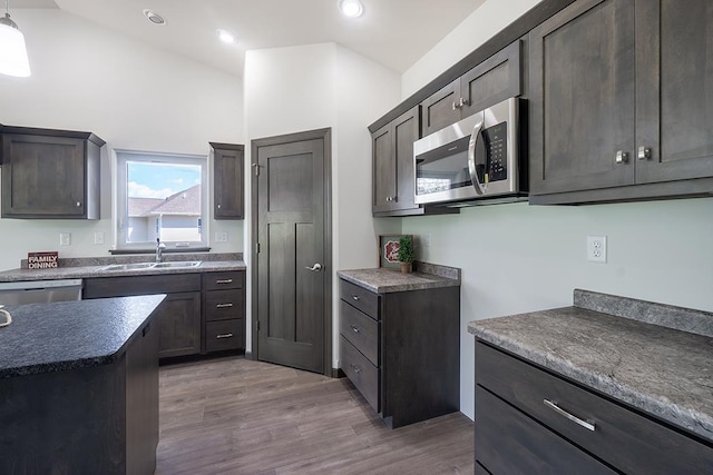 kitchen featuring dark brown cabinetry, sink, stainless steel appliances, vaulted ceiling, and light wood-type flooring