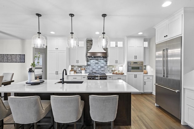 kitchen with pendant lighting, appliances with stainless steel finishes, sink, white cabinets, and an island with sink