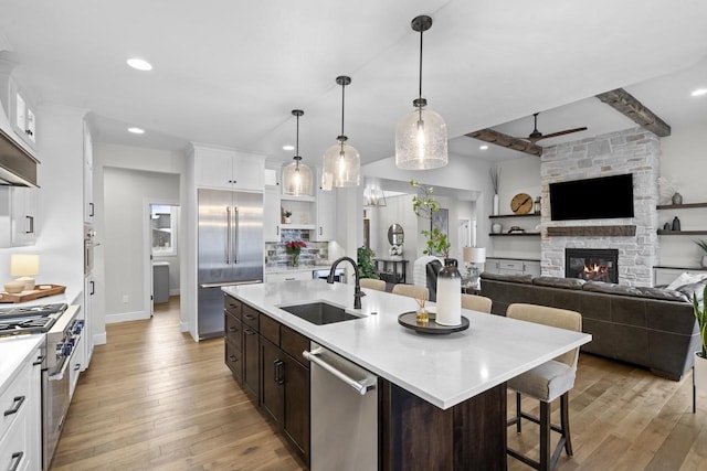 kitchen with beamed ceiling, premium appliances, sink, decorative light fixtures, and an island with sink