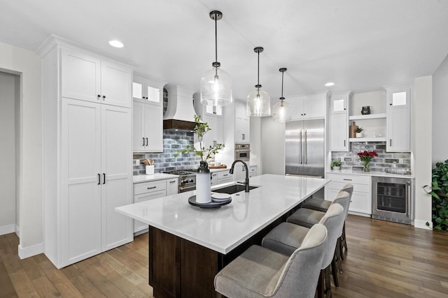 kitchen with premium appliances, white cabinetry, wine cooler, and an island with sink