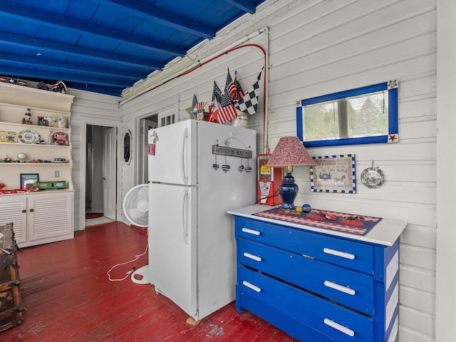 kitchen featuring dark wood-type flooring, white refrigerator, blue cabinets, wooden walls, and beam ceiling