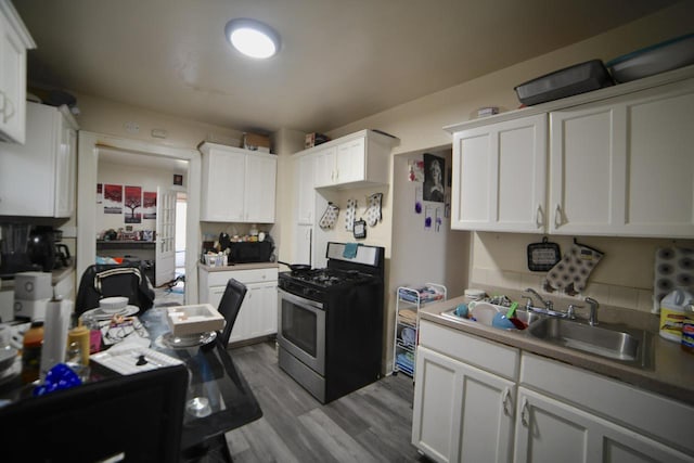4828 N 25th St, Milwaukee, WI 53209 - kitchen with stainless steel gas range, a sink, white cabinets, wood finished floors, and decorative backsplash