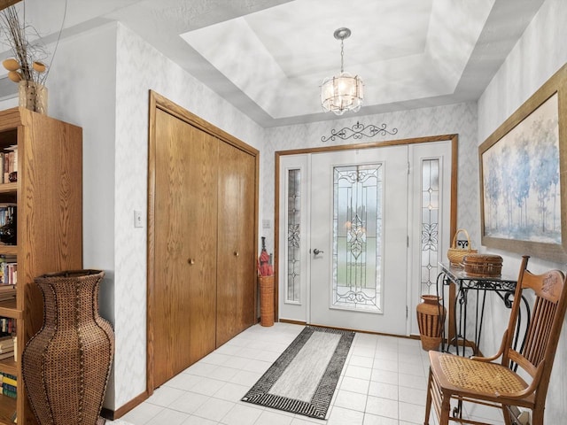 entryway with light tile patterned floors, a tray ceiling, and a notable chandelier