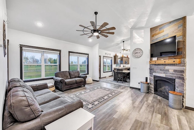 living room featuring ceiling fan, a large fireplace, vaulted ceiling, and light hardwood / wood-style flooring