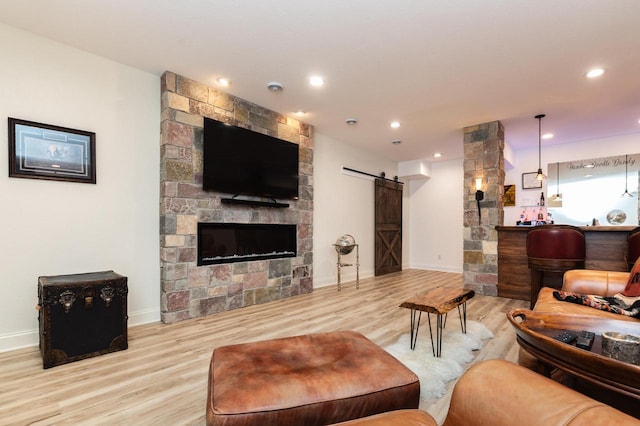 living room featuring a barn door, a stone fireplace, and light wood-type flooring