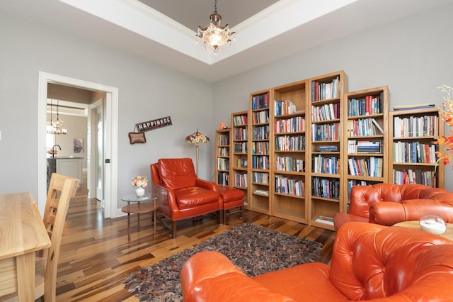 living area featuring a raised ceiling, crown molding, hardwood / wood-style floors, and a chandelier