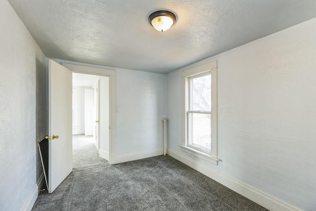 unfurnished room featuring a textured ceiling and dark colored carpet