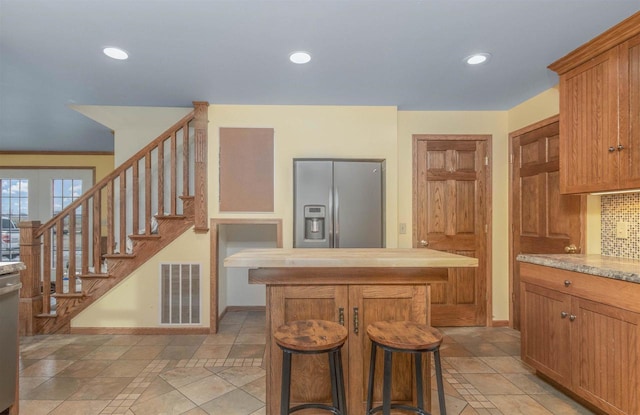 kitchen featuring a center island, stainless steel refrigerator with ice dispenser, decorative backsplash, light tile patterned flooring, and a kitchen bar