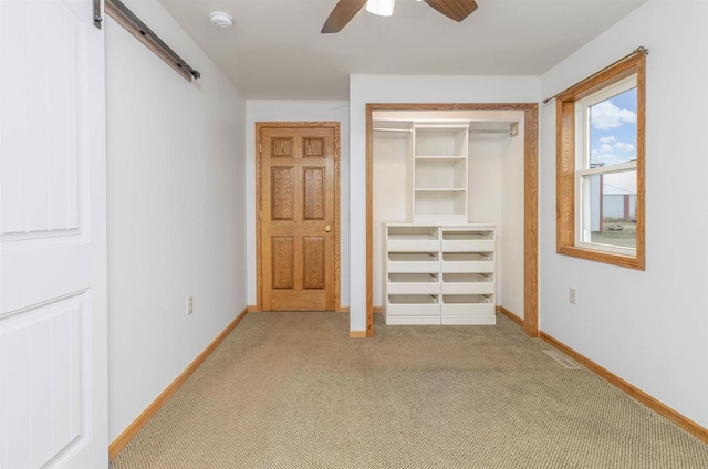 unfurnished bedroom featuring a barn door, ceiling fan, and light carpet