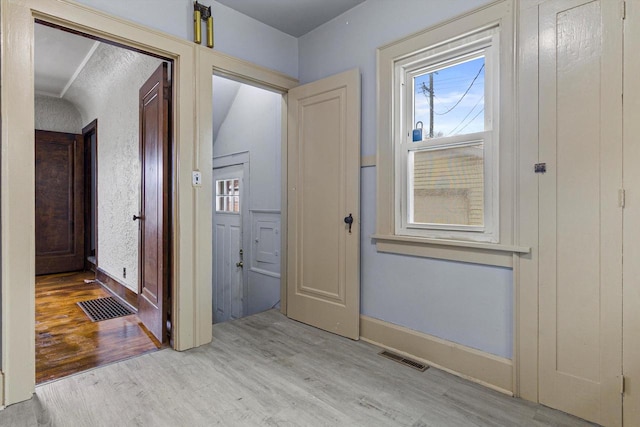 corridor with light hardwood / wood-style floors and vaulted ceiling