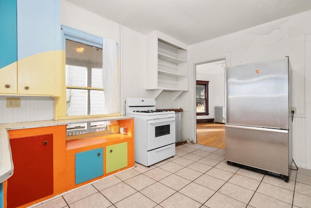 kitchen with white gas stove, stainless steel fridge, light tile patterned flooring, and radiator heating unit