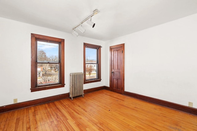 empty room featuring rail lighting, light hardwood / wood-style flooring, and radiator