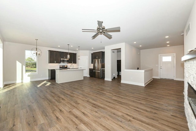 unfurnished living room with ceiling fan with notable chandelier, a stone fireplace, and dark hardwood / wood-style flooring