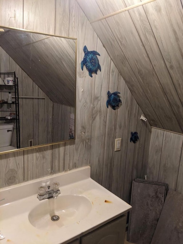 bathroom featuring vanity, wood walls, and vaulted ceiling