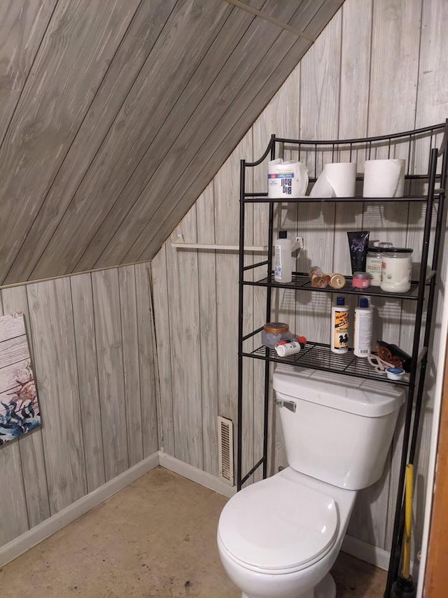 bathroom featuring wood walls, concrete flooring, vaulted ceiling, and toilet