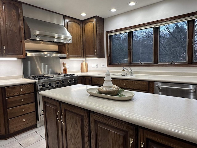 kitchen with appliances with stainless steel finishes, wall chimney exhaust hood, dark brown cabinetry, sink, and light tile patterned floors