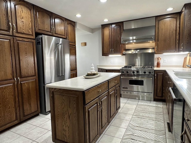 kitchen featuring dark brown cabinets, stainless steel appliances, wall chimney range hood, a center island, and light tile patterned flooring