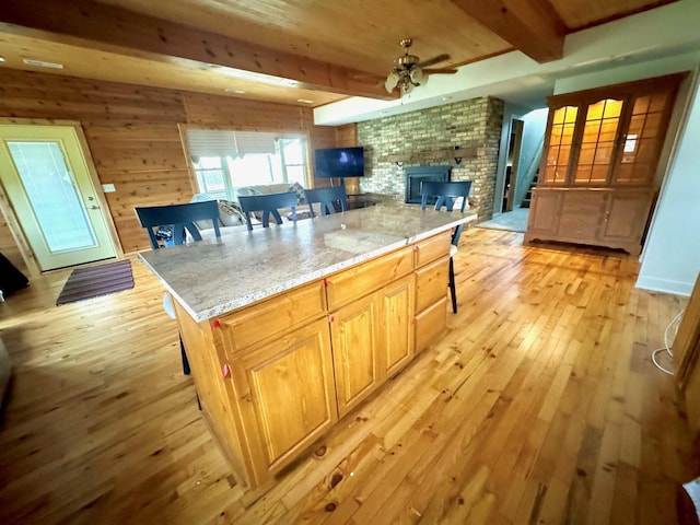 kitchen with beam ceiling, a wood stove, a kitchen breakfast bar, wooden walls, and light wood-type flooring