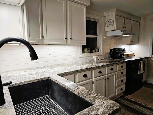 kitchen featuring dark wood-type flooring, sink, decorative backsplash, light stone countertops, and black / electric stove