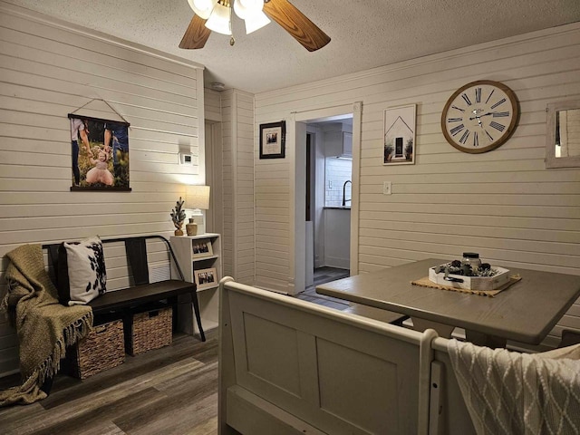 interior space with a textured ceiling, ceiling fan, dark wood-type flooring, and wood walls