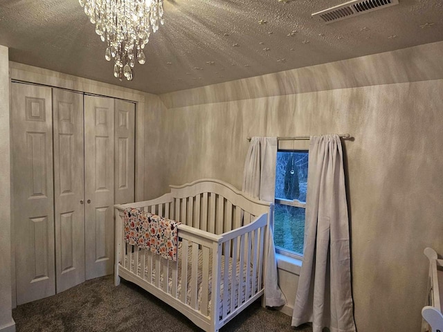 carpeted bedroom featuring a chandelier, a crib, a textured ceiling, and a closet