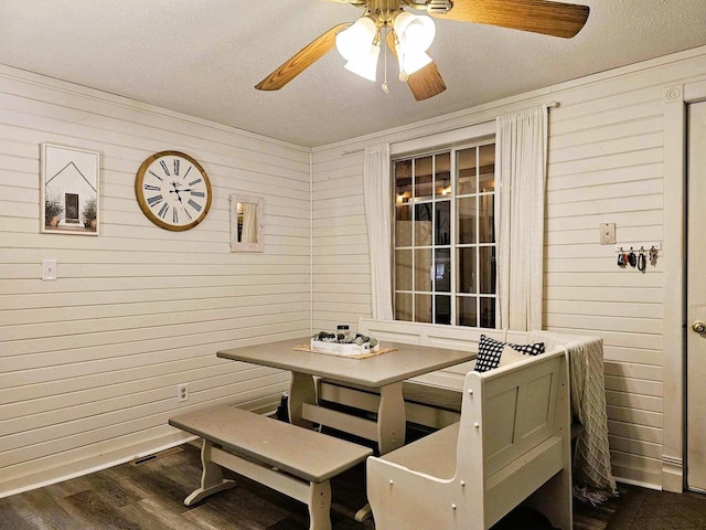 dining room with wood walls, ceiling fan, dark wood-type flooring, and a textured ceiling