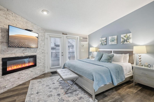 bedroom featuring lofted ceiling, access to outside, a stone fireplace, a textured ceiling, and dark wood-type flooring