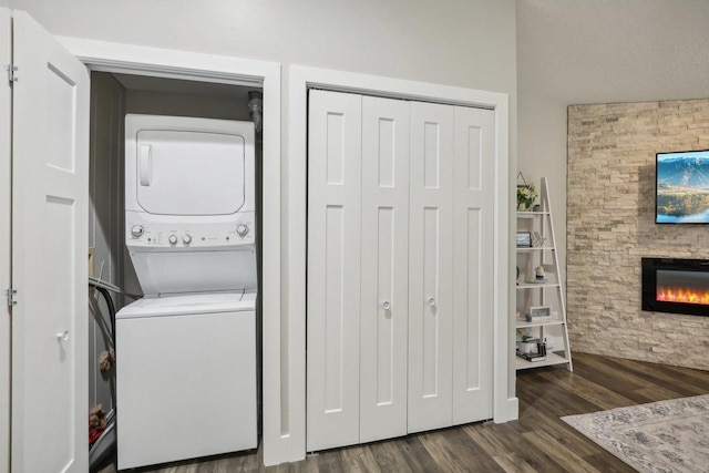 laundry area featuring dark hardwood / wood-style flooring, a stone fireplace, and stacked washer / drying machine