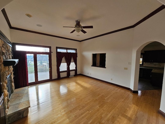 unfurnished living room featuring light hardwood / wood-style floors, a stone fireplace, ceiling fan, and ornamental molding