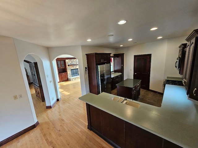 kitchen with appliances with stainless steel finishes, dark brown cabinets, light hardwood / wood-style flooring, a fireplace, and a center island