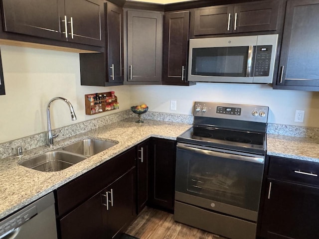 kitchen featuring light stone counters, light hardwood / wood-style flooring, sink, appliances with stainless steel finishes, and dark brown cabinetry