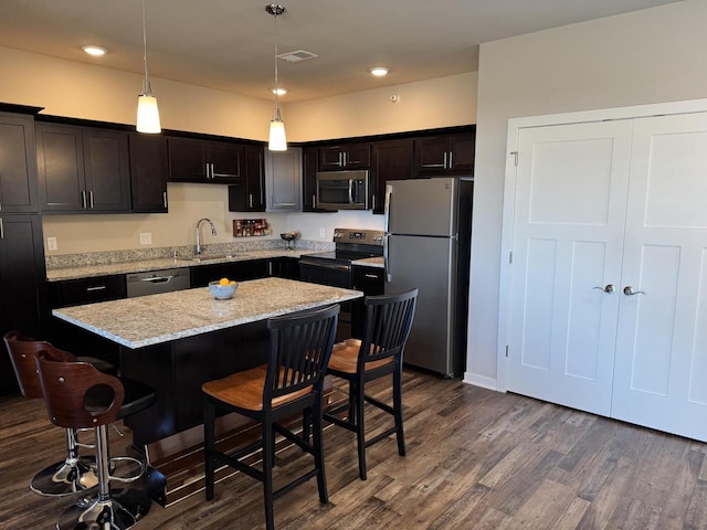 kitchen with decorative light fixtures, a kitchen island, appliances with stainless steel finishes, a kitchen breakfast bar, and sink