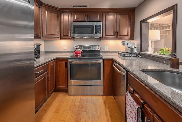 kitchen featuring dark stone counters, stainless steel appliances, light hardwood / wood-style floors, and sink