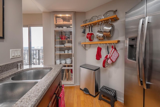 kitchen with stainless steel fridge, light stone counters, light hardwood / wood-style flooring, and sink