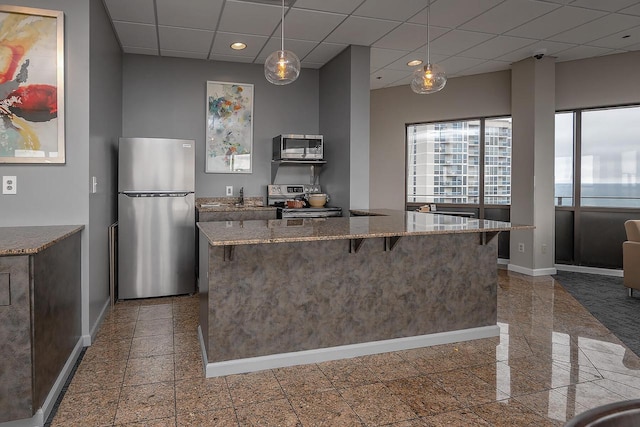 kitchen featuring light stone countertops, a drop ceiling, hanging light fixtures, stainless steel appliances, and a kitchen bar