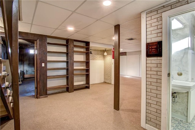 basement featuring light carpet, a drop ceiling, and brick wall