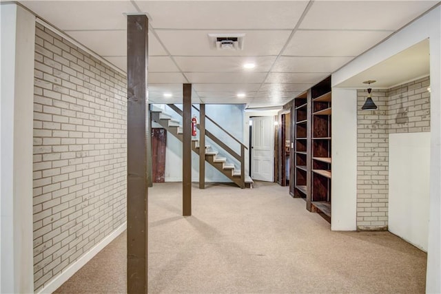 basement featuring carpet floors, a drop ceiling, and brick wall