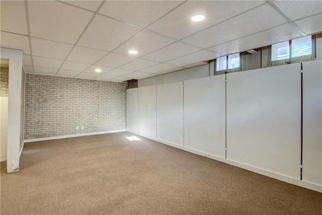 basement featuring carpet flooring, a drop ceiling, and brick wall