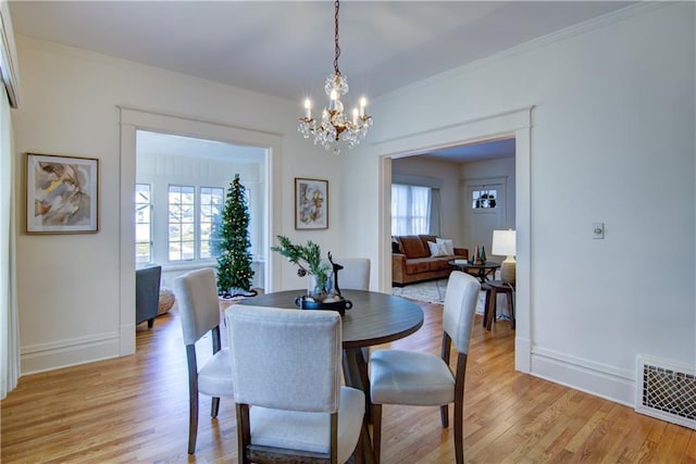 dining area featuring light wood-type flooring, crown molding, and a chandelier